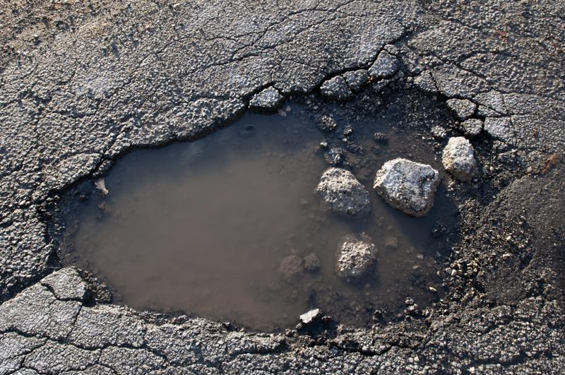 A pothole fills with muddy water.
