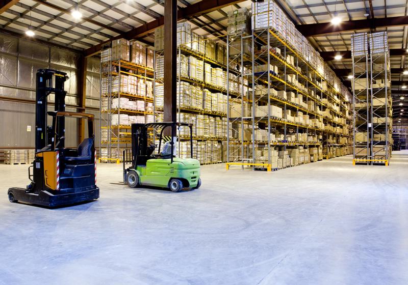 Two forklifts drive through a warehouse.