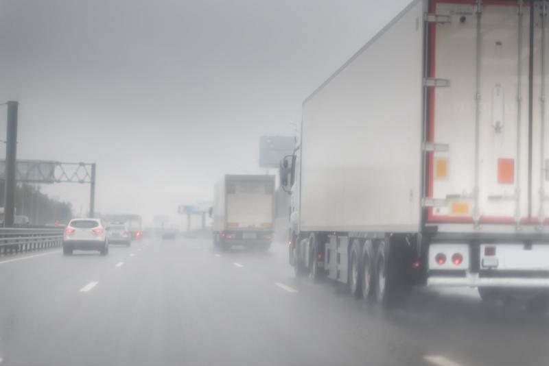 A semitruck drives down a highway in the snow.