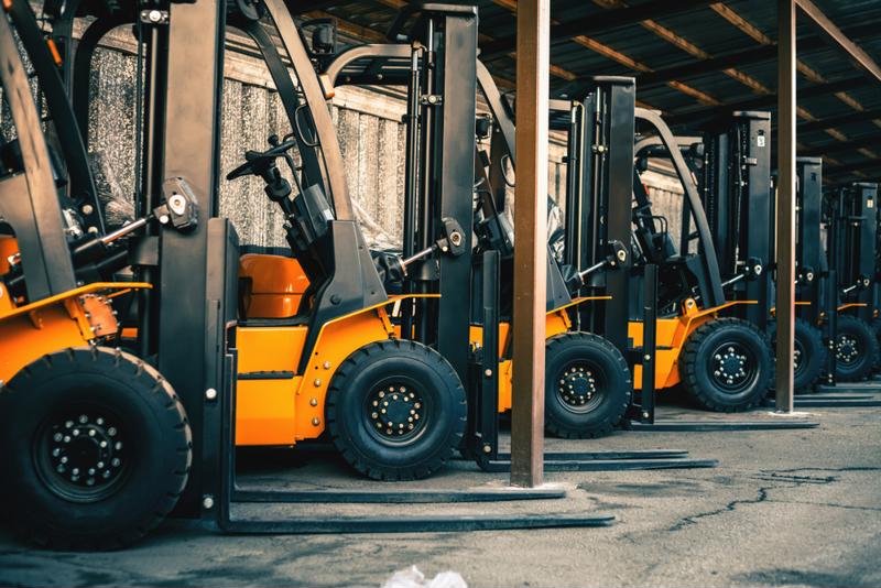 A fleet of forklifts are parked in a warehouse.