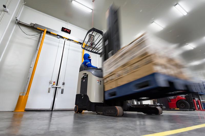A forklift operator drives a pallet of goods through a cold storage facility.
